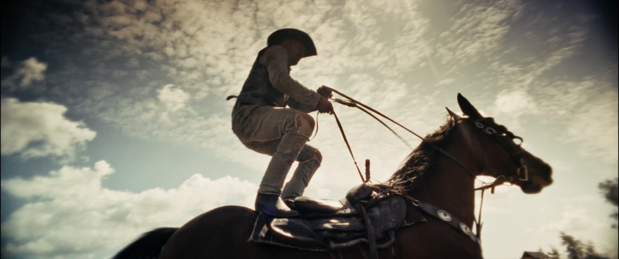 Low-angle silhouette of a rider crouched on the saddle of a galloping horse against a bright sky - Amon Amarth